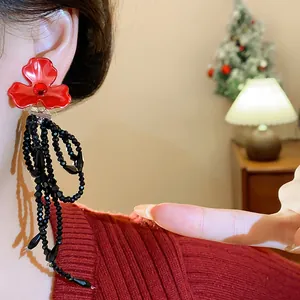 Close-up of elegant red flower earrings with long black beaded tassels on a model.