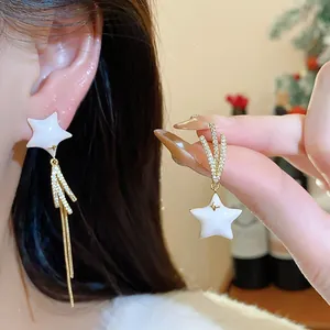 Detailed shot of asymmetrical gold-plated star earrings with zircon tassels and white enamel