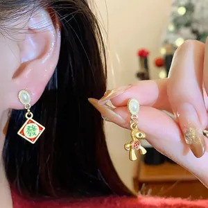 Detail shot of asymmetric gold New Year earrings with horse and mahjong charms on model.