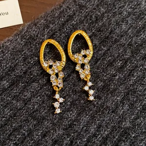 Nahaufnahme eleganter goldener Quastenohrringe mit funkelnden weißen Strasssteinen und Textur
