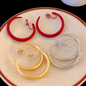 Dettaglio di eleganti orecchini a clip a forma di C in finiture rosso, oro e argento.