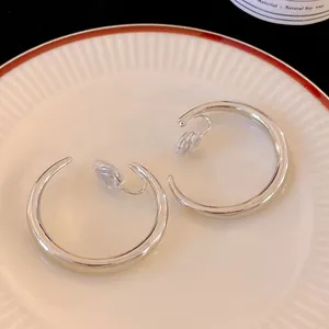 Dettaglio orecchini a clip argento a forma di C su piatto di ceramica bianca