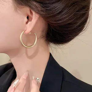 Primo piano di un orecchino a clip a forma di C in oro opaco minimalista indossato