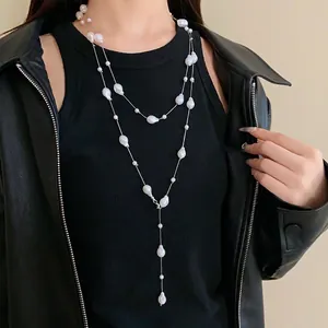 French minimalist long necklace with layered irregular imitation pearls on black outfit.
