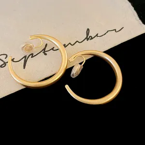 Dettaglio macro di orecchini a clip a forma di C in oro opaco con cuscinetti morbidi.