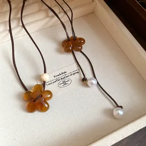 Macro detail of amber resin flower and white pearl charms on brown necklace cord.