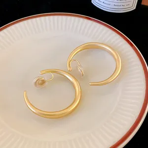 Dettaglio ravvicinato di orecchini a clip a forma di C in oro opaco su un piatto di porcellana