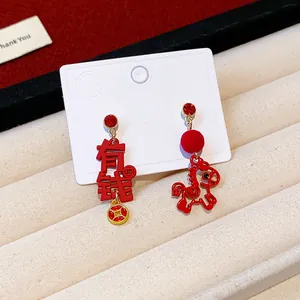 Detail shot of red asymmetric earrings with horse charm and "Rich" character pendant.