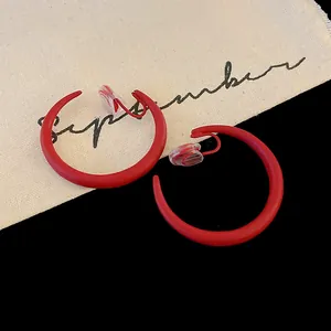 Primo piano di orecchini a clip rossi a forma di C con finitura opaca e stile minimal.