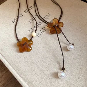 Detailed view of amber resin flower pendant necklace with dark brown cord and pearls.