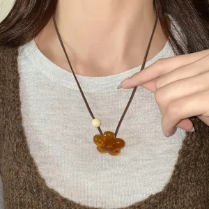 Detail view of a translucent amber resin flower pendant necklace on a brown cord.