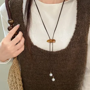Detail view of a resin flower pendant necklace with pearl accents on a brown vest