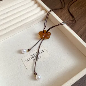 Macro detail of amber resin flower pendant and pearl accents on cord necklace.