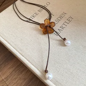 Detailed view of the amber resin flower pendant and pearls on a brown cord