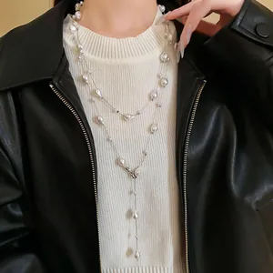 Detailed shot of long layered faux pearl necklace worn over a white ribbed sweater.