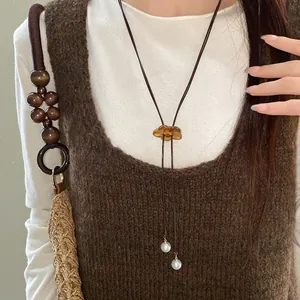 Elegant resin flower pendant necklace with faux pearl charms worn on a brown knit dress