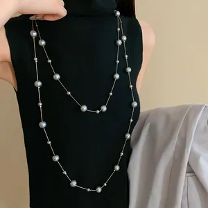 Elegant long faux pearl necklace with grey beads and thin gold chain on black top
