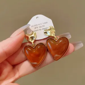 Close-up detail of retro Maillard amber resin heart drop earrings with gold finish