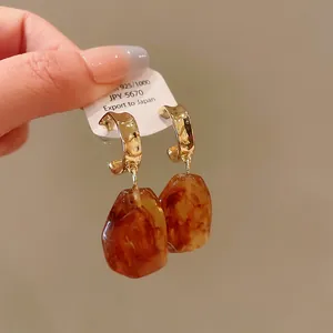 Close-up of retro Maillard style drop earrings with amber resin and 925 silver needles.