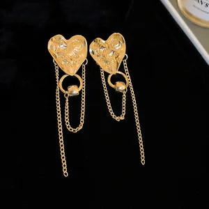 Close-up of gold heart earrings with chain tassels and engraved 'Have a Heart' text