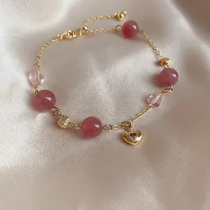 Detailed macro view of synthetic strawberry quartz beads and gold heart charm bracelet
