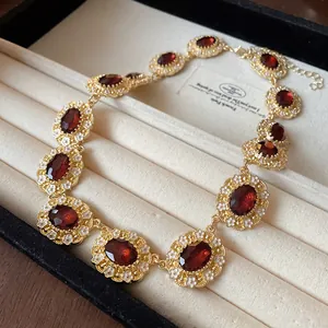 Close-up detail of vintage gold necklace with oval red gemstones and white flowers in a jewelry box