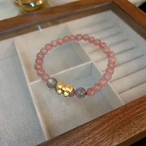 Close-up detail of a pink synthetic strawberry quartz bracelet with a gold bow charm