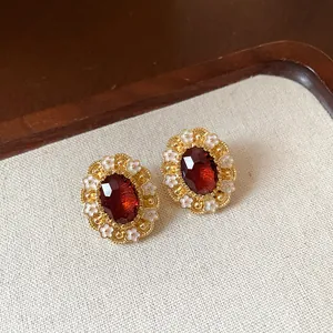 Detailed macro view of vintage oval gold-tone earrings with red gemstone and white enamel flowers