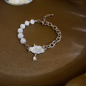 Detail of fashion bracelet with white cat's eye beads and unique cloud pendant design.