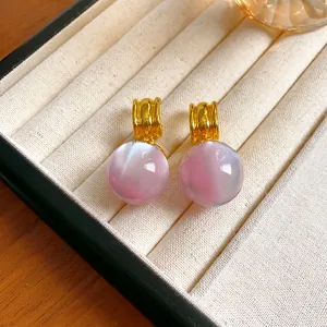 Close-up of pink pearlescent resin sphere earrings with irregular golden studs on a tray.