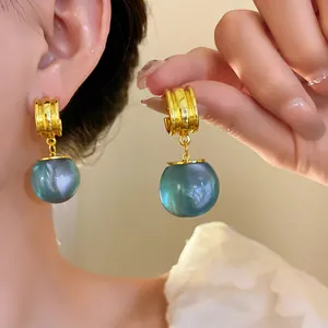 Close-up of elegant gold and teal resin drop earrings worn on the model's ear for detail