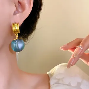 Close-up of blue resin geometric drop earrings with gold finish on model's ear