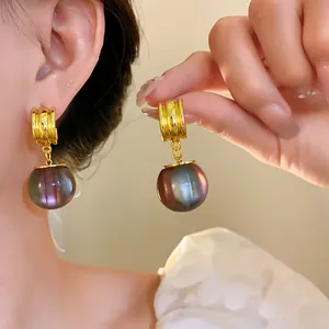 Close-up view of irregular gold-tone earrings with iridescent purple resin ball pendant