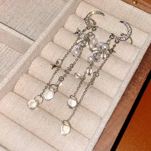 Close-up of silver-tone tassel earrings with moon, stars, and pearls in a jewelry box