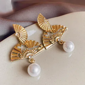 Close-up macro view of gold fan-shaped stud earrings with elegant white pearl drops and crystals.
