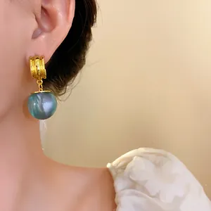 Close-up shot of elegant gold plated earrings featuring a blue-grey resin sphere pendant