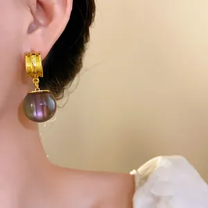 Detailed view of elegant gold drop earrings with iridescent purple resin spheres