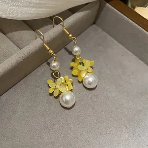 Detailed view of handmade yellow floral earrings with elegant pearls on a gray jewelry tray