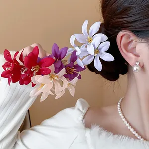 Close-up of colorful fabric flower hairpins held by a model with elegant pearl jewelry.