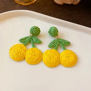 Macro view of handmade woven raffia cherry earrings in yellow and green