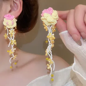 Detailed view of handmade crochet flower earrings with long white beaded tassels worn by a model