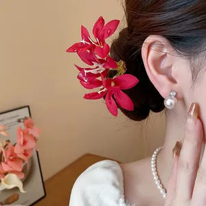 Elegant red fabric flower hair pin detail styled in a bun with pearl necklace and earring