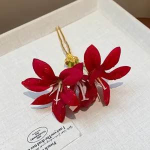 Close-up of red fabric flower hairpin with delicate water droplets on petals.