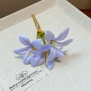 Close-up of purple fabric flower hairpin with golden prongs and water drop detail.