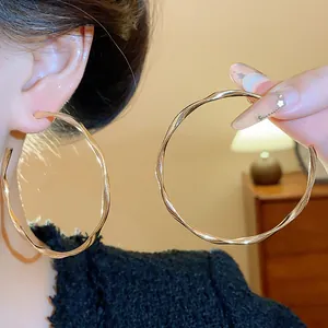 Large gold-toned twisted hoop earrings shown on ear and held to demonstrate the scale
