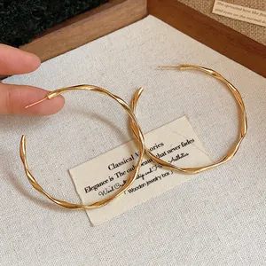 Close-up detail of stylish large gold twisted hoop earrings featuring elegant texture