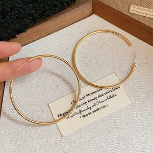 Elegant large gold-tone minimalist hoop earrings displayed on a rustic wooden jewelry tray