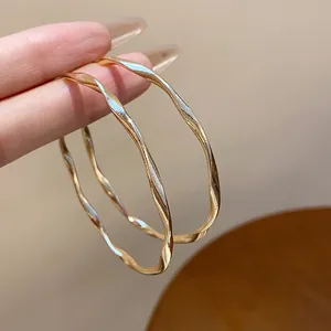 Detailed view of elegant large gold-tone twisted hoop earrings held by a hand model.