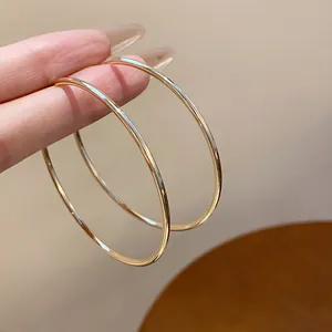 Close-up view of minimalist large gold hoop earrings being held by hand on warm background