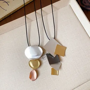 Detail shot of two geometric necklaces with metallic oval and square pendants on tray